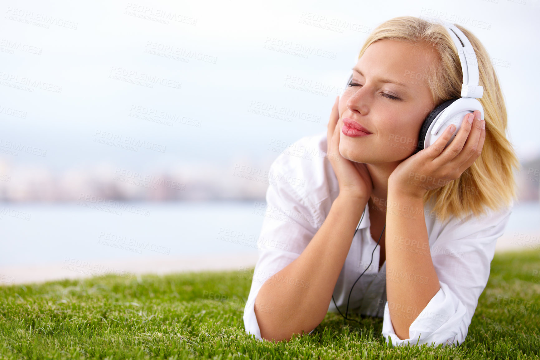 Buy stock photo Shot of a woman lying on a grassy field listening to music with her eyes closed