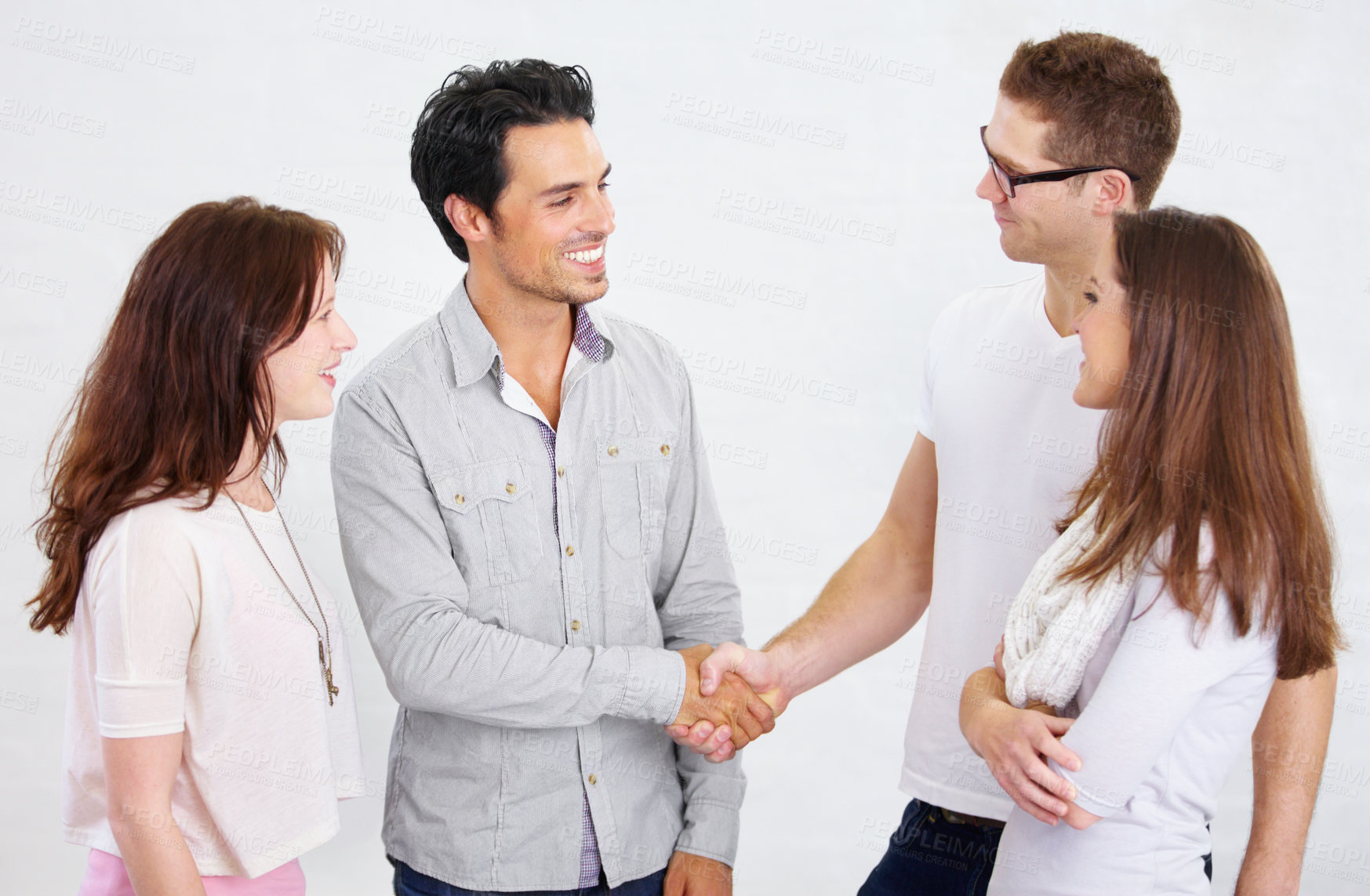 Buy stock photo Shot of a two young business professionals shaking hands while their coworkers look on