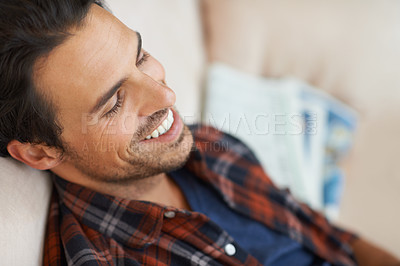 Buy stock photo A handsome young man lying down on a sofa at home and laughing to himself