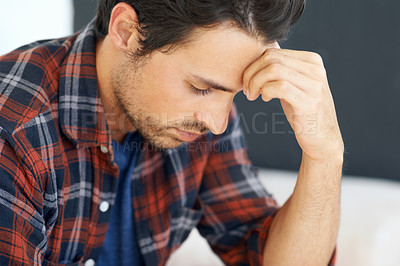 Buy stock photo Profile of a gorgeous young man sitting on a sofa and looking down with hand rested against his forehead and an expression of concern on his face