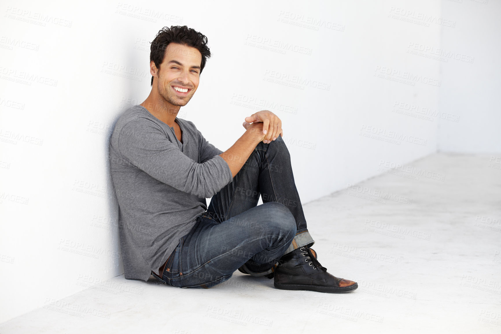 Buy stock photo Smile, fashion and portrait of young man by a white wall in empty room with casual, cool and trendy outfit. Happy, confidence and handsome male model from Canada sitting on floor with edgy style.
