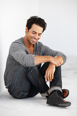 Buy stock photo Smile, fashion and handsome young man by white wall with casual, cool and trendy outfit. Happy, confident and attractive male model from Canada sitting on floor with edgy style and positive attitude.
