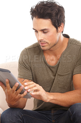 Buy stock photo A handsome young man using his digital tablet while sitting on the sofa at home