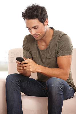 Buy stock photo A handsome young man sitting on his sofa and typing a text message