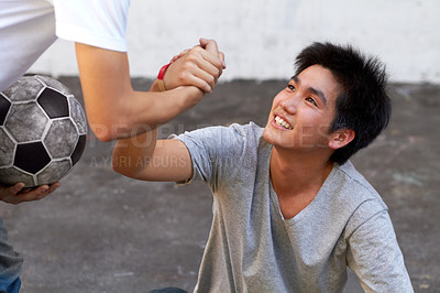 Buy stock photo Asian boy helping his friend up from the ground during a soccer game