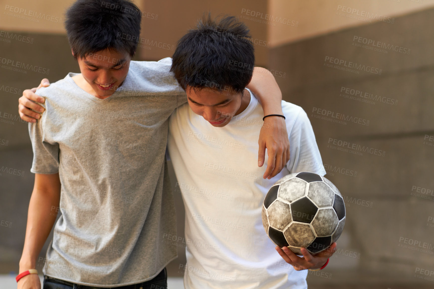 Buy stock photo Two asian boys walking with their arms around eachother holding a soccer ball