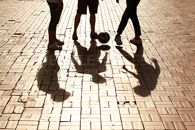 Buy stock photo Sports, football and shadow of friends with a ball training for a skill, trick or stunt on a pavement. Silhouette, soccer and legs of people practicing for a game, match or tournament in the city.