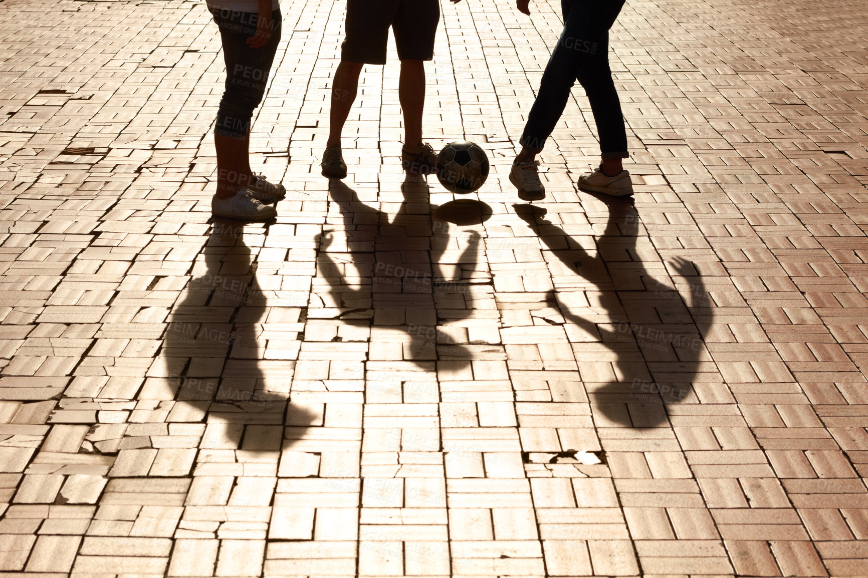 Buy stock photo Sports, football and shadow of friends with a ball training for a skill, trick or stunt on a pavement. Silhouette, soccer and legs of people practicing for a game, match or tournament in the city.