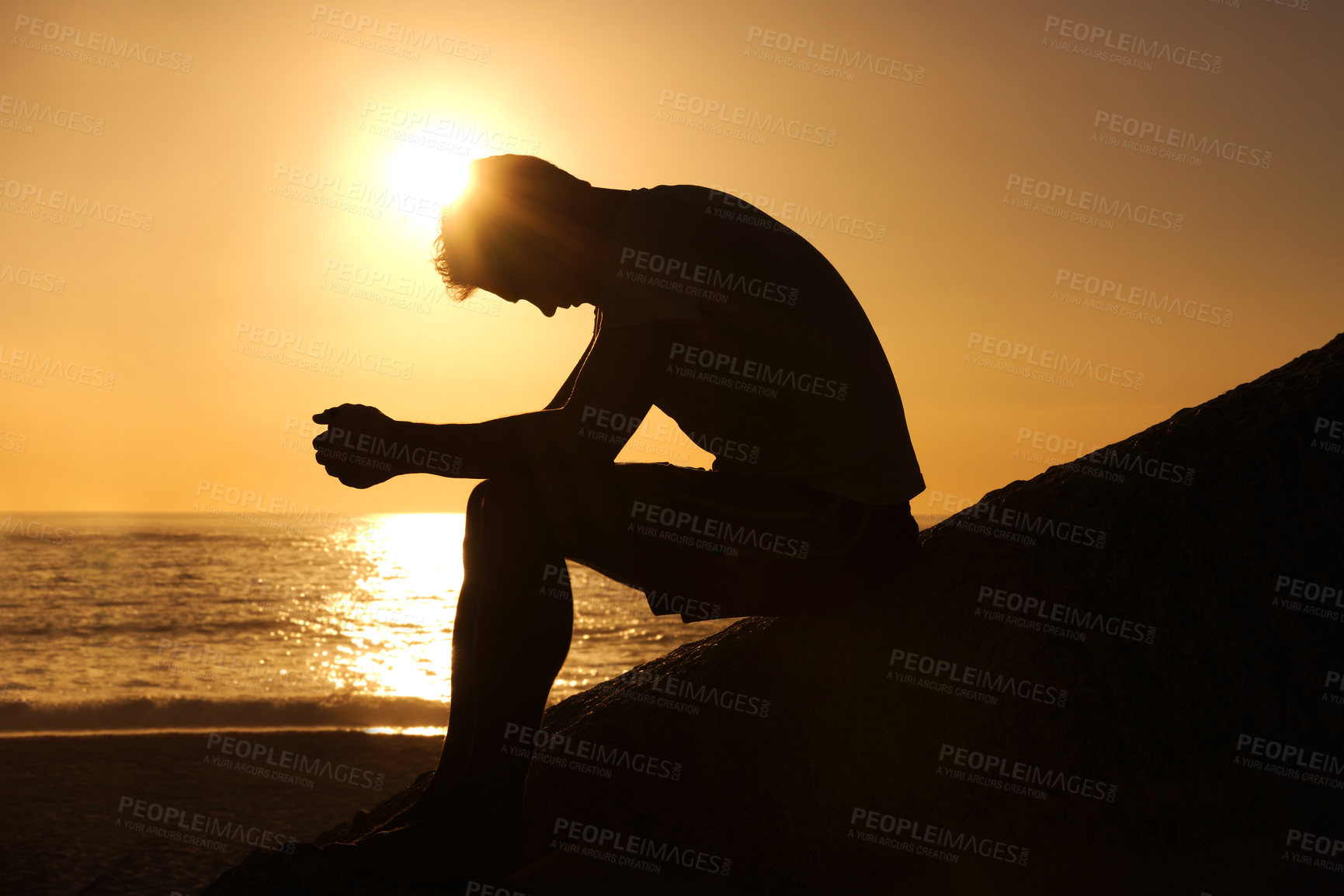 Buy stock photo Silhouette of a man sitting by the ocean and contemplating while looking downwards