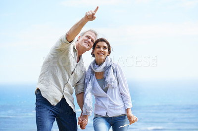 Buy stock photo Happy couple, pointing and travel together at the beach with love, happiness and adventure in summer. Retirement, vacation and mature man and woman holding hands and sightseeing at ocean on holiday
