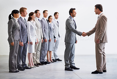 Buy stock photo A young businessman welcoming a new employee to the company as colleagues look on