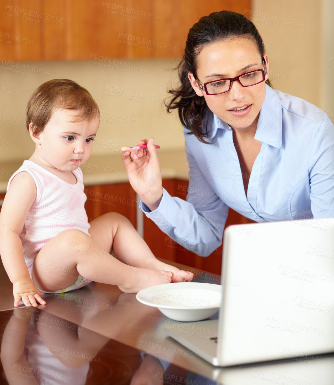 Buy stock photo Shot of a single mom feeding her baby while trying to work on her laptop