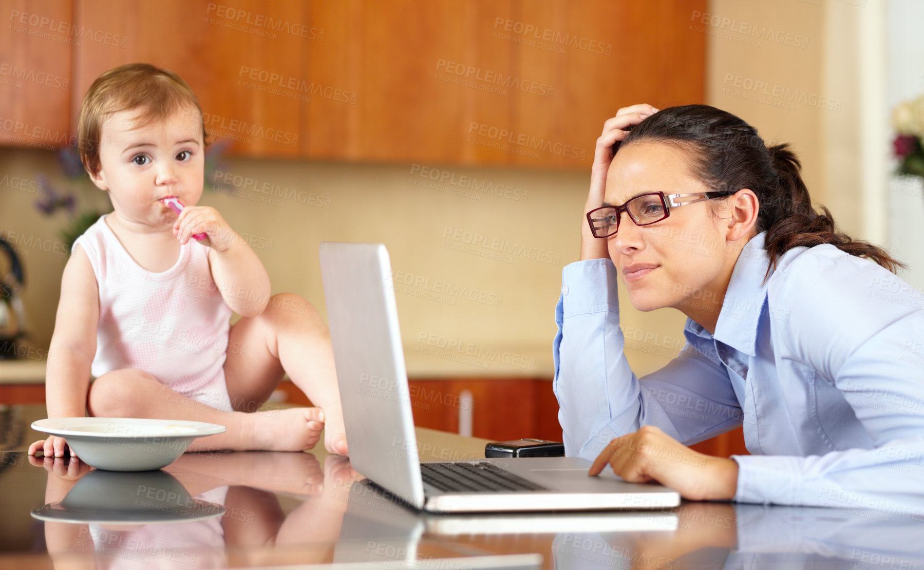 Buy stock photo Shot of an overworked  mom working at her laptop with her baby sitting on the counter