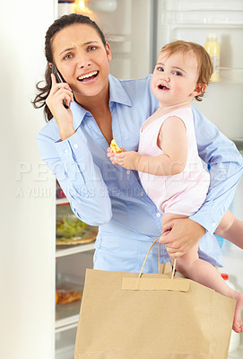 Buy stock photo An overwhelmed working mom speaking on the phone while holding her baby and a bag of groceries