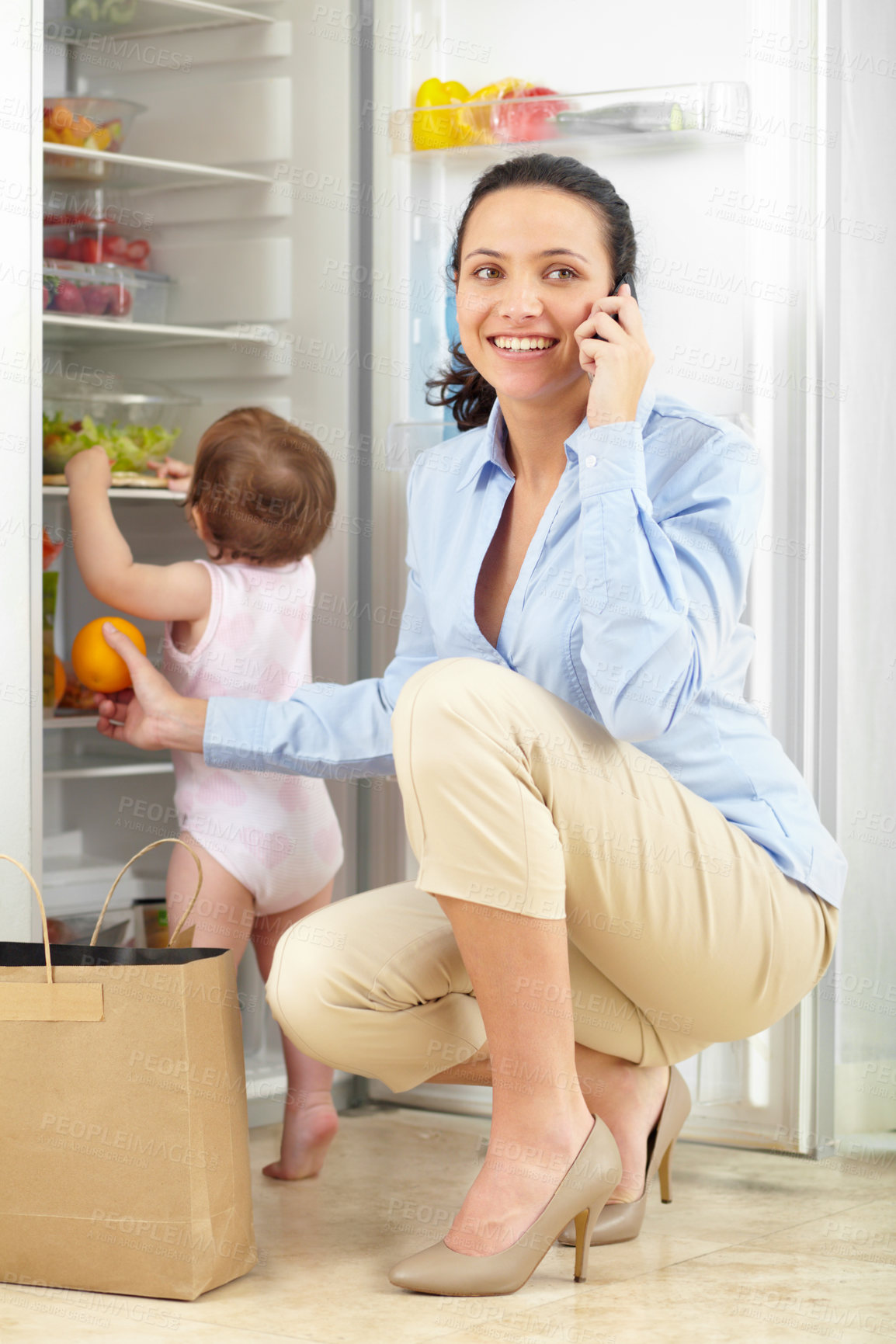 Buy stock photo Phone call, grocery and mother in home with kid at fridge in kitchen, conversation and smile. Smartphone, happy mom and fruit, orange and family packing food in refrigerator with child in connection