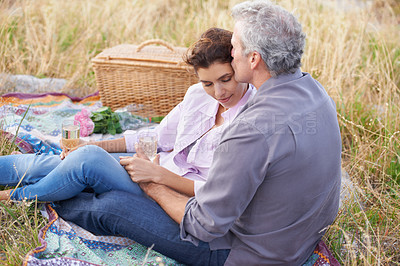 Buy stock photo Couple, kiss and relax at picnic on grass with wine, drinks and celebration on date in park. Love, man and woman with food, basket and flowers for marriage anniversary or outdoor in nature on holiday