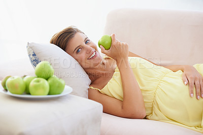 Buy stock photo A happy pregnant woman relaxing on her couch and enjoying an apple