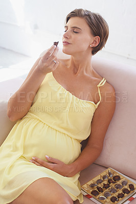 Buy stock photo A young pregnant woman enjoying a box of chocolates all to herself