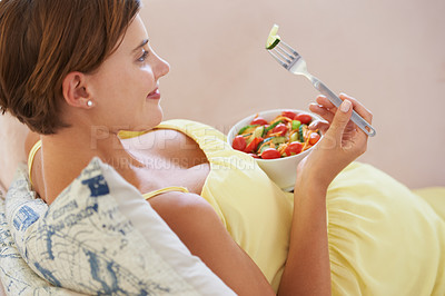 Buy stock photo A young pregnant woman enjoying a healthy salad while relaxing on the couch