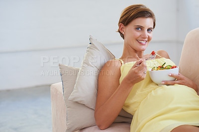 Buy stock photo Portrait of a young pregnant woman enjoying a healthy salad while relaxing on the couch