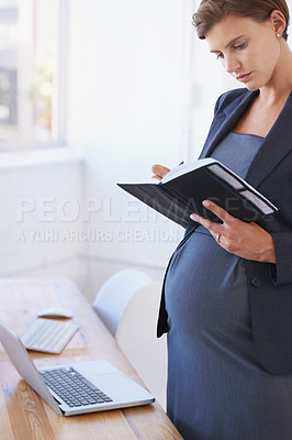 Buy stock photo A pregnant businesswoman reading her daily planner in her office