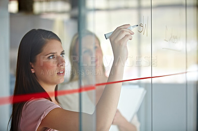 Buy stock photo A young businesswoman writing down plans on a glass pane
