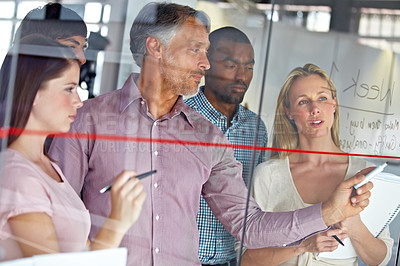 Buy stock photo A group of business colleagues brainstorming together at a glass wall