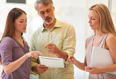 Buy stock photo Shot of three business professionals standing and going through some paperwork together