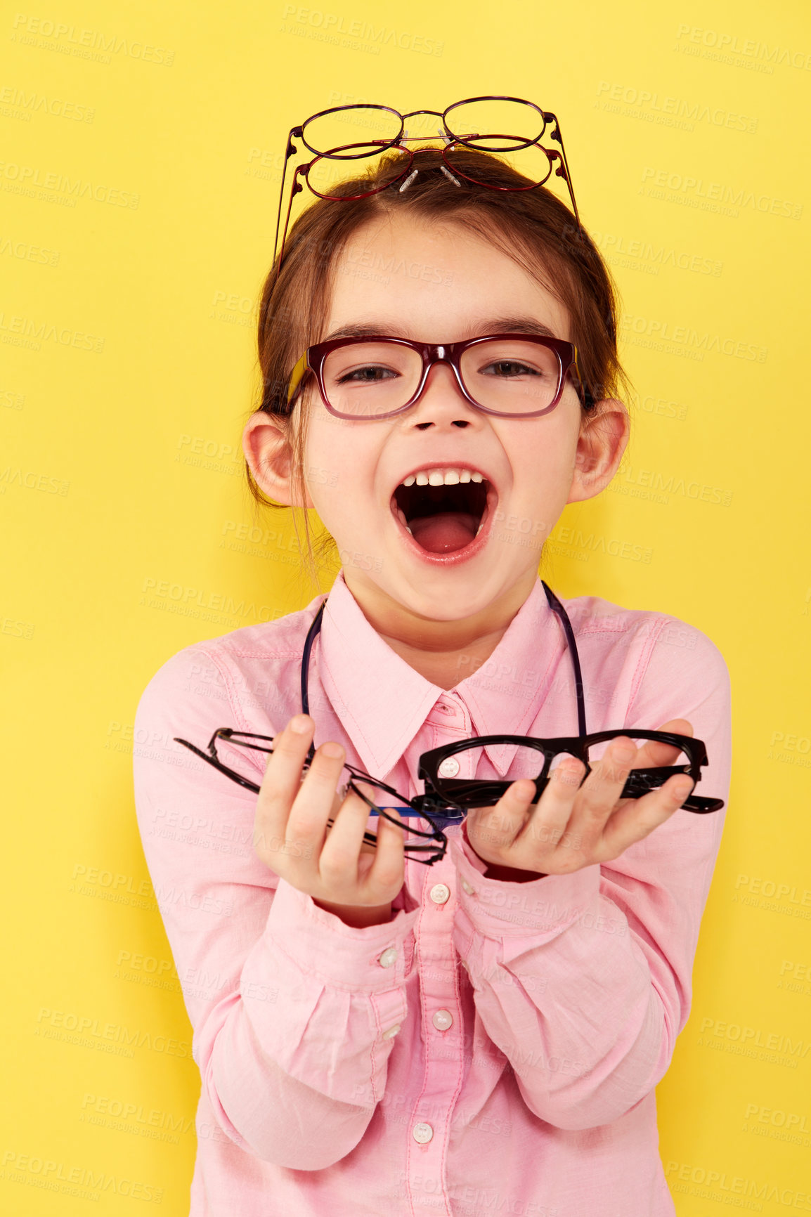 Buy stock photo A cute little girl standing against a yellow background with a hand full of glasses