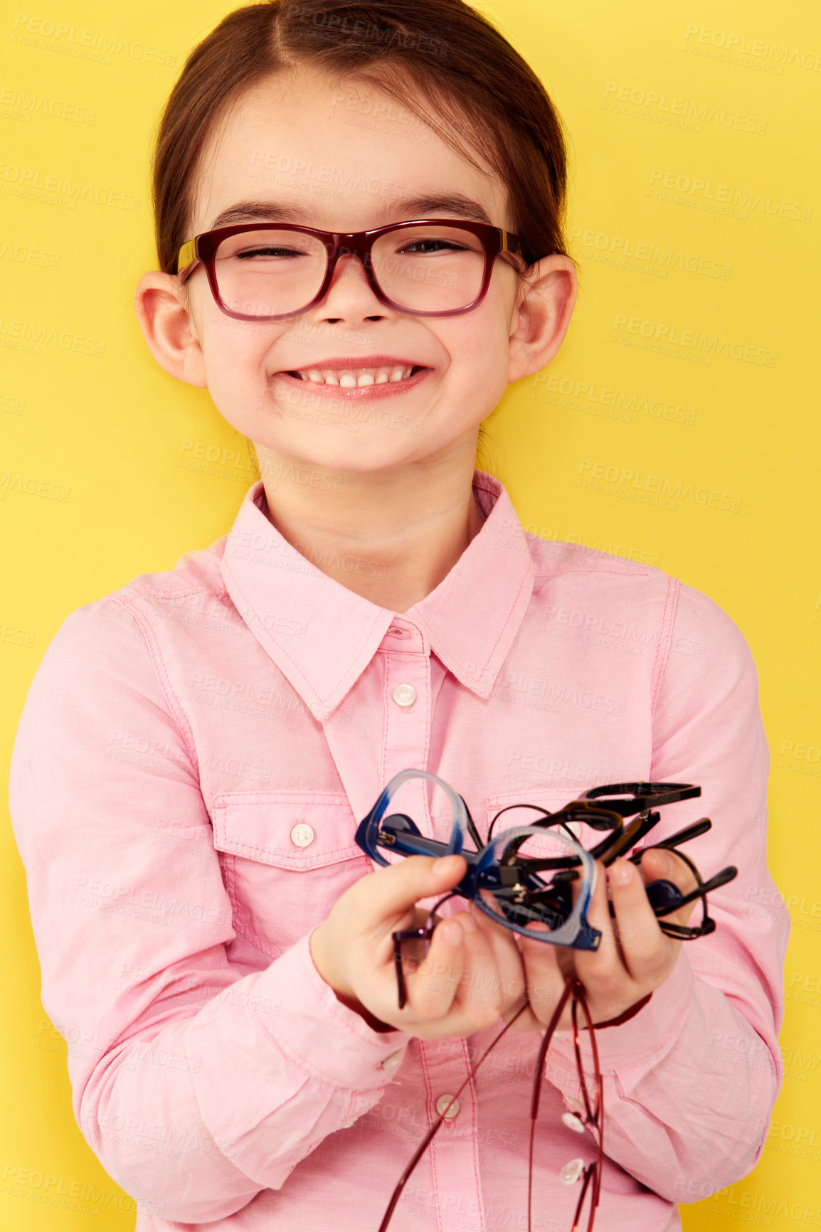 Buy stock photo A cute little girl standing against a yellow background with a hand full of glasses
