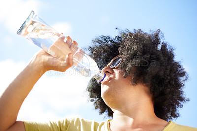 Buy stock photo Man, drinking and water with blue sky outdoor for concert, event or wellness with sunglasses and afro. Person, hydration and beverage in summer for relax, thirsty or enjoyment with sunshine in nature