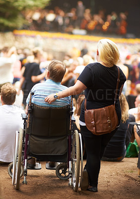 Buy stock photo Rear view of a wife standing beside her husband who is sitting in his wheelchair at a live music event