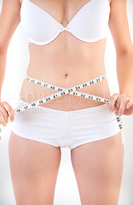 Buy stock photo A young woman in her underwear with a measuring tape wrapped around her stomach