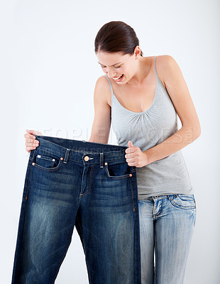 Buy stock photo A pretty, slim woman holding up a pair of her old oversized jeans