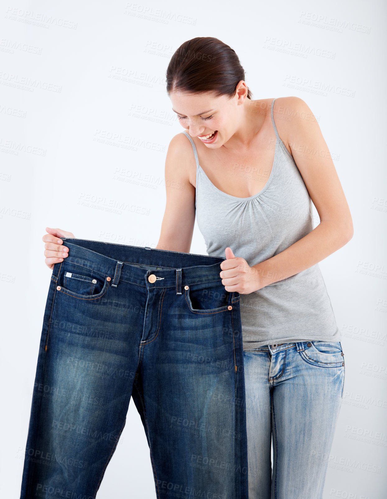 Buy stock photo A pretty, slim woman holding up a pair of her old oversized jeans