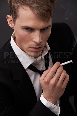 Buy stock photo Face, thinking and a man smoking a cigarette in studio on a dark background for tobacco addiction. Nicotine, habit and unhealthy with a young person in a suit, taking a break from business to smoke