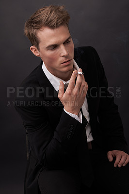 Buy stock photo A handsome young man in a suit smoking a cigarette