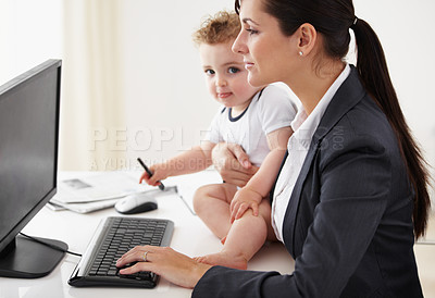 Buy stock photo Working mother holding a baby while working on her computer