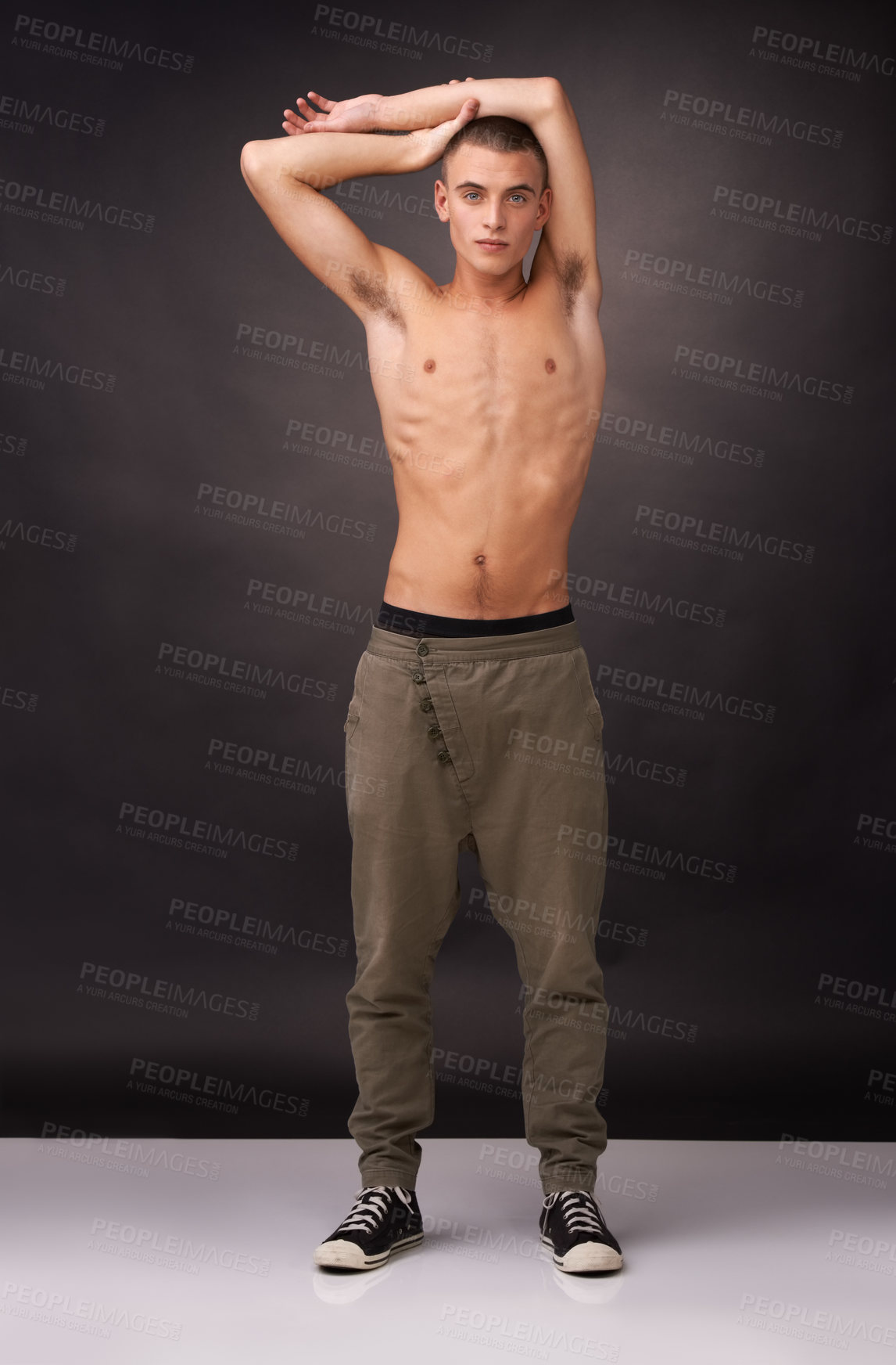 Buy stock photo Portrait, fashion and a shirtless young man in studio on a gray background for casual masculine style. Fitness, confident and the macho or manly body of a serious model in trendy pants and sneakers