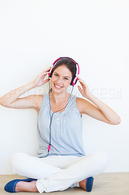 Buy stock photo Portrait, music and woman on a floor with headphones in studio, happy and streaming on a wall background. Face, smile and girl relax with podcast, radio or audio track while sitting against mockup
