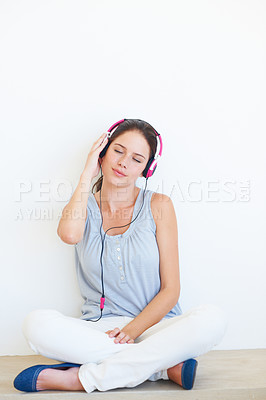 Buy stock photo Relax, music and woman on a floor with headphones in studio, happy and streaming on a wall background. Zen, feeling and girl with wellness podcast, radio or audio track while sitting against mockup