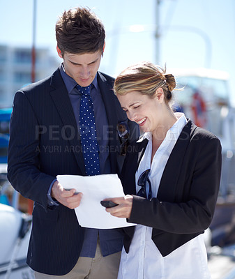 Buy stock photo Young businesspeople looking over some paperwork at the marina