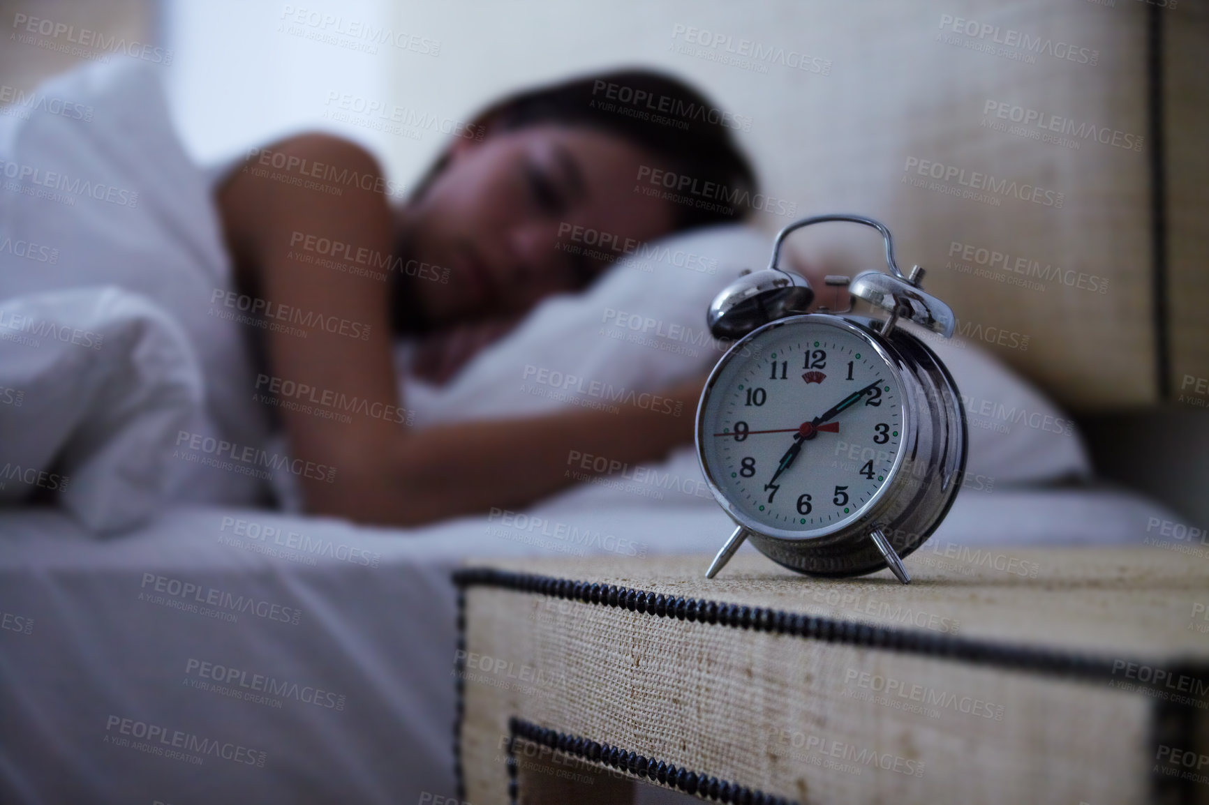 Buy stock photo A young woman sleeping with her alarm clock next to her bed