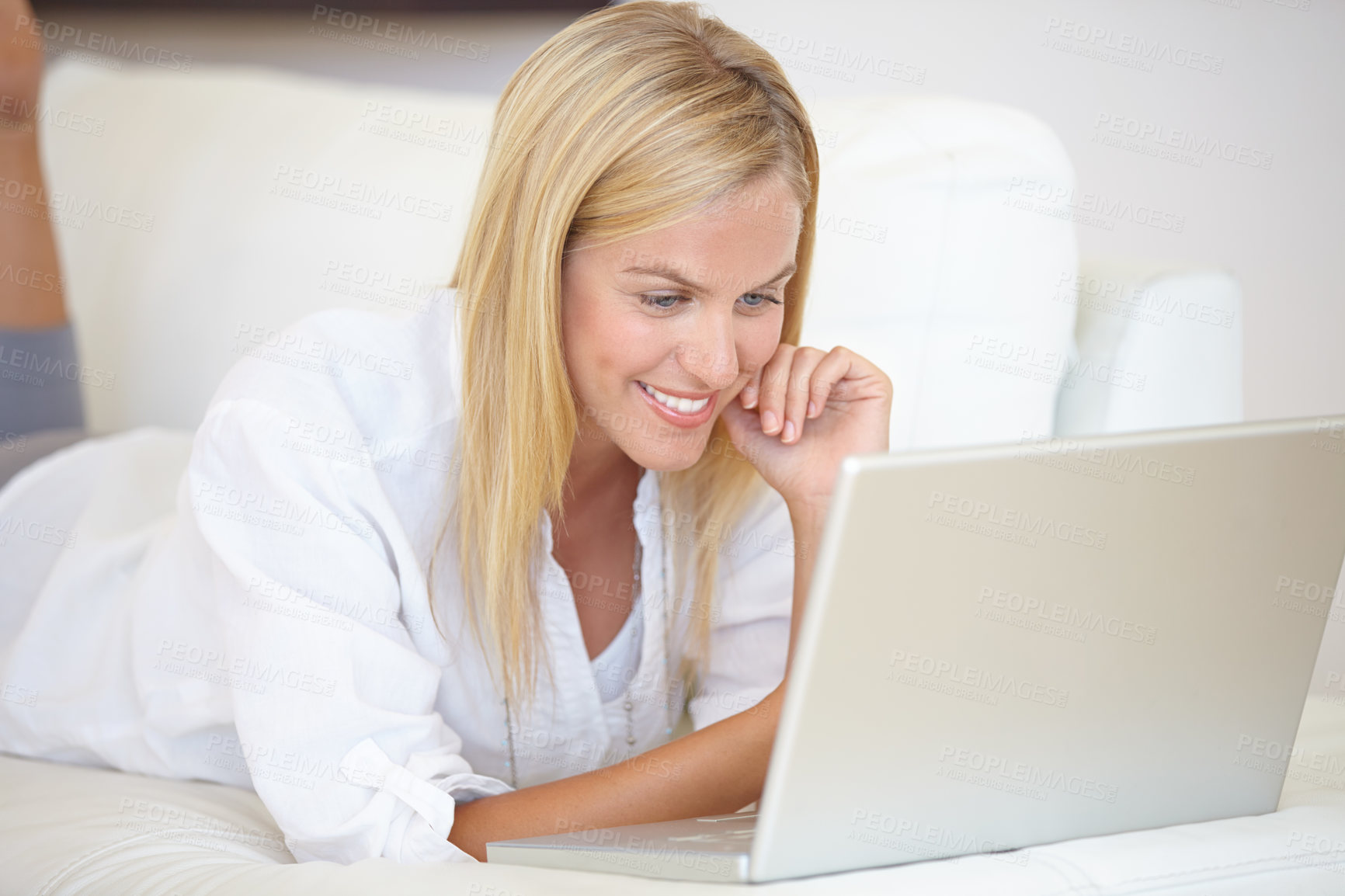 Buy stock photo A gorgeous young woman working on her laptop while lying on the sofa