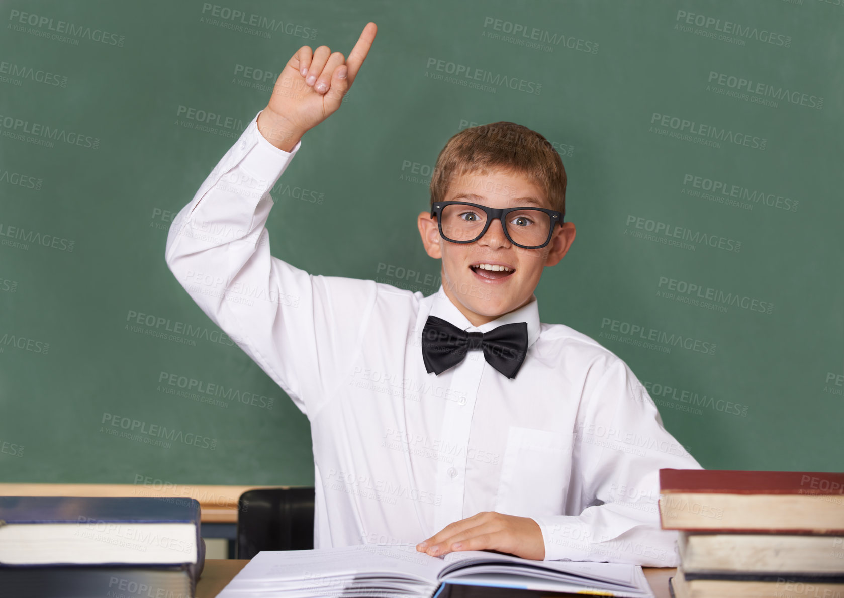 Buy stock photo Boy child, books and raised hand in portrait with smile for question, information and knowledge on classroom. Student kid, happy and excited for education, learning and development by chalkboard