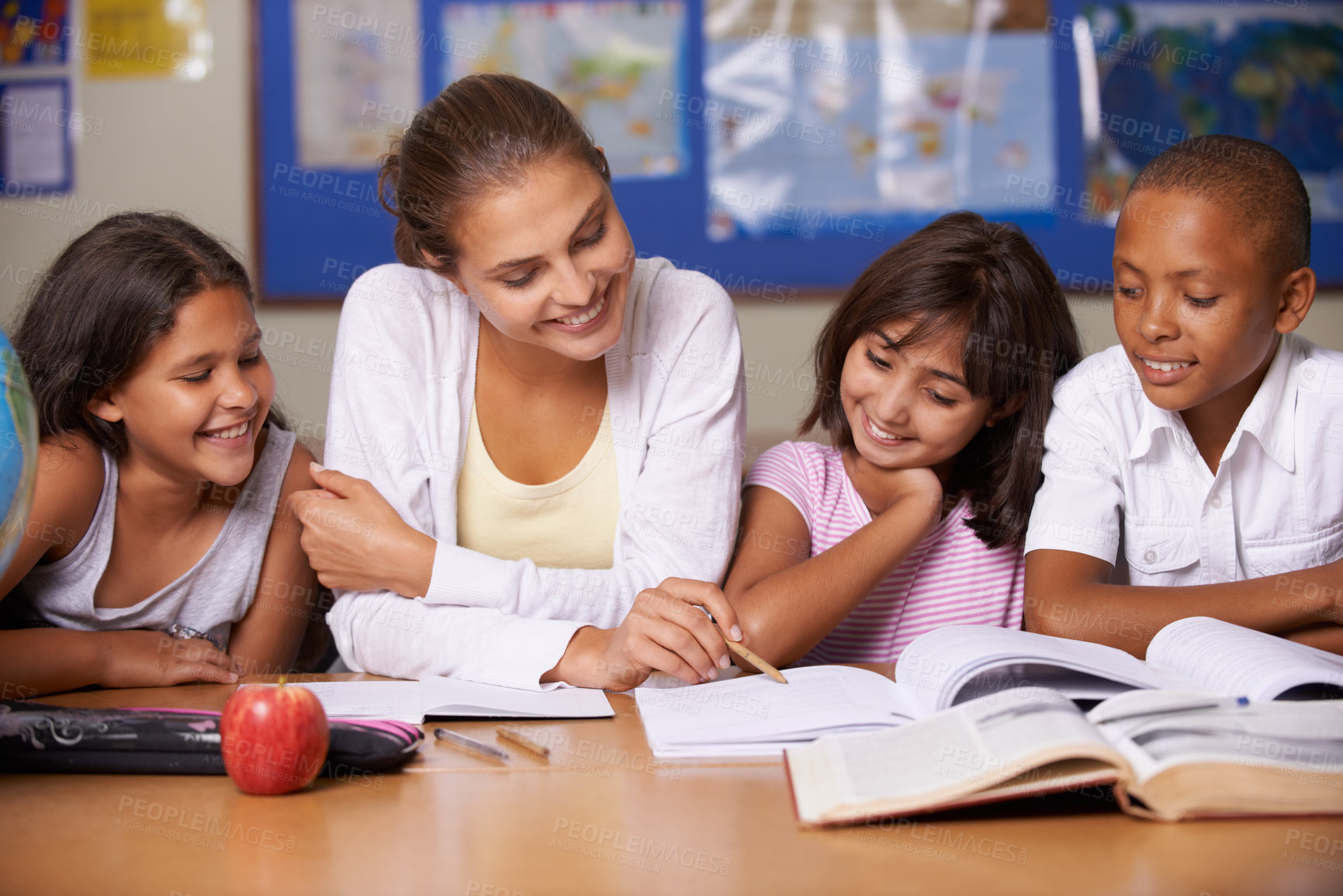 Buy stock photo A young teacher sitting with her three ethnic pupils reading through a textbook