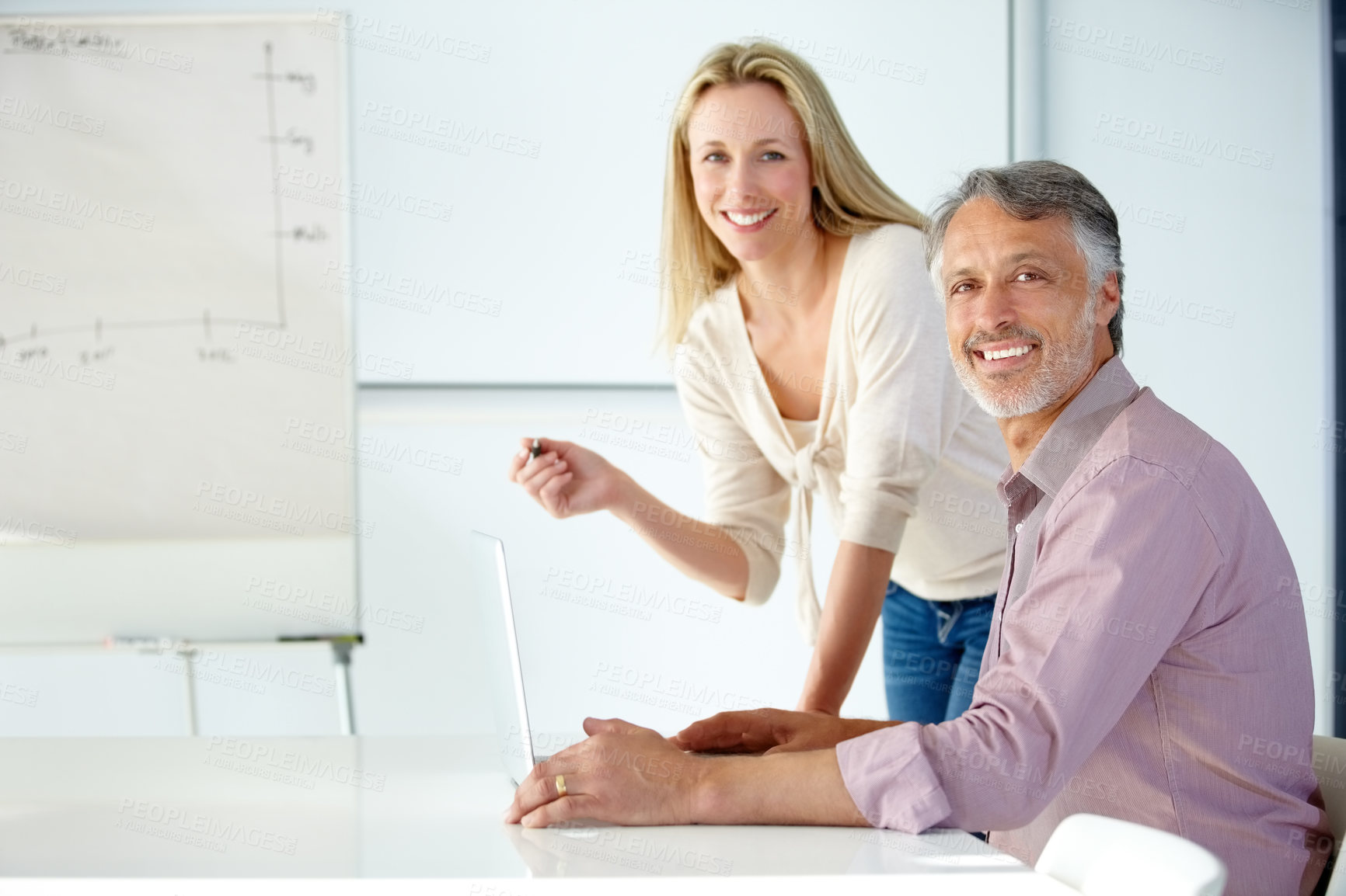 Buy stock photo Two smiling coworkers discussing business in a meeting using a flip chart and laptop - Portrait