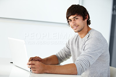 Buy stock photo Young man smiling while using a laptop at a desk