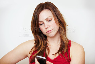 Buy stock photo An annoyed young woman looking at her cellphone