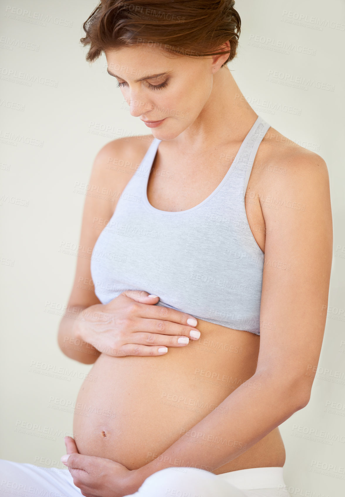 Buy stock photo A beautiful young pregnant woman looking down at her bare tummy